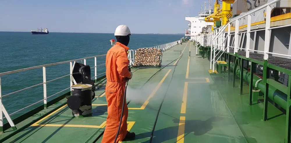 Crew member in orange coveralls working on a ship's deck at sea