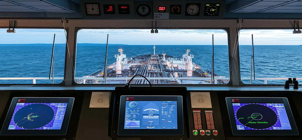 Ship's bridge with navigation displays, looking forward over the deck to the sea