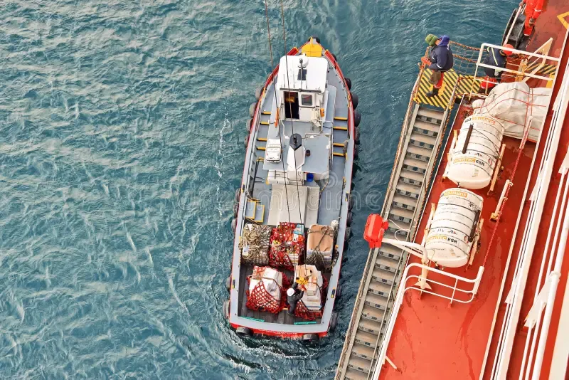 Aerial view of a supply boat alongside a vessel, with stores transferred up the gangway