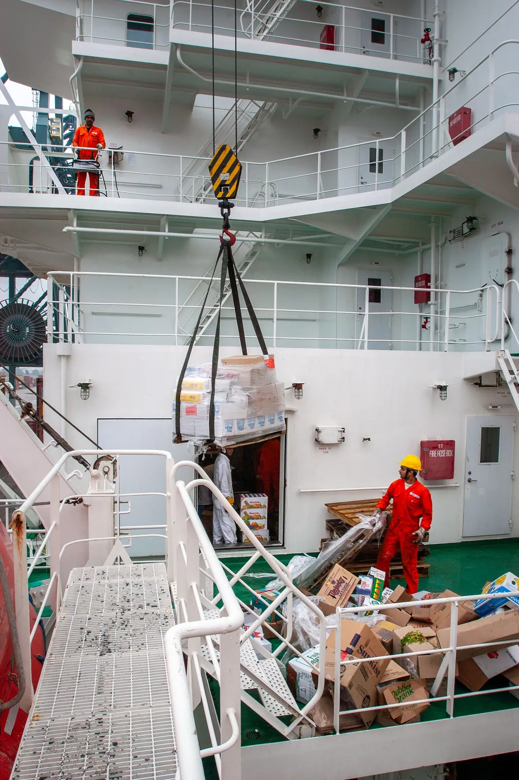 Ship's crane lifting stores aboard a vessel alongside the quay